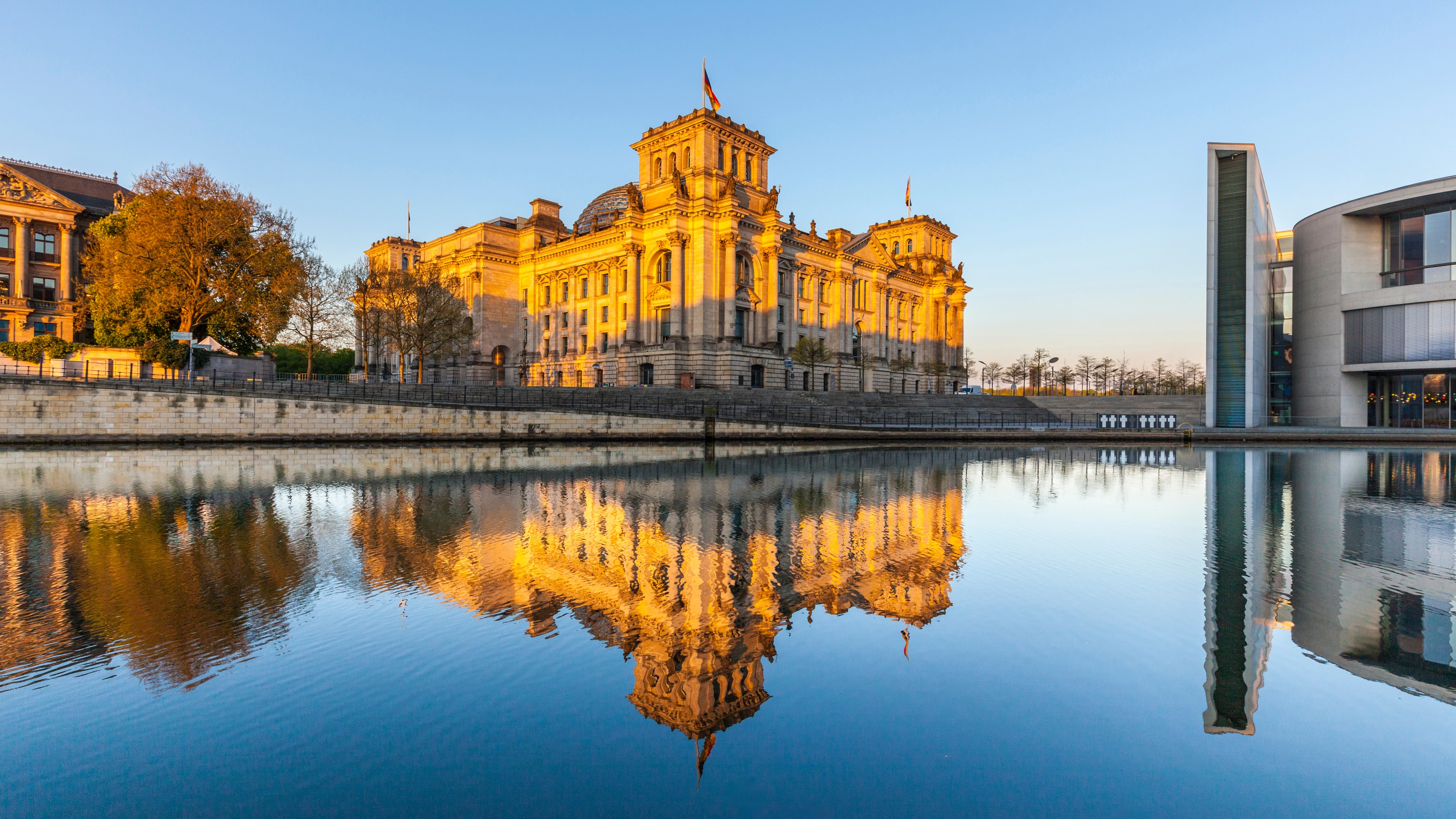 Das Berliner Reichstagsgebäude spiegelt sich im Fluss bei Sonnenuntergang.