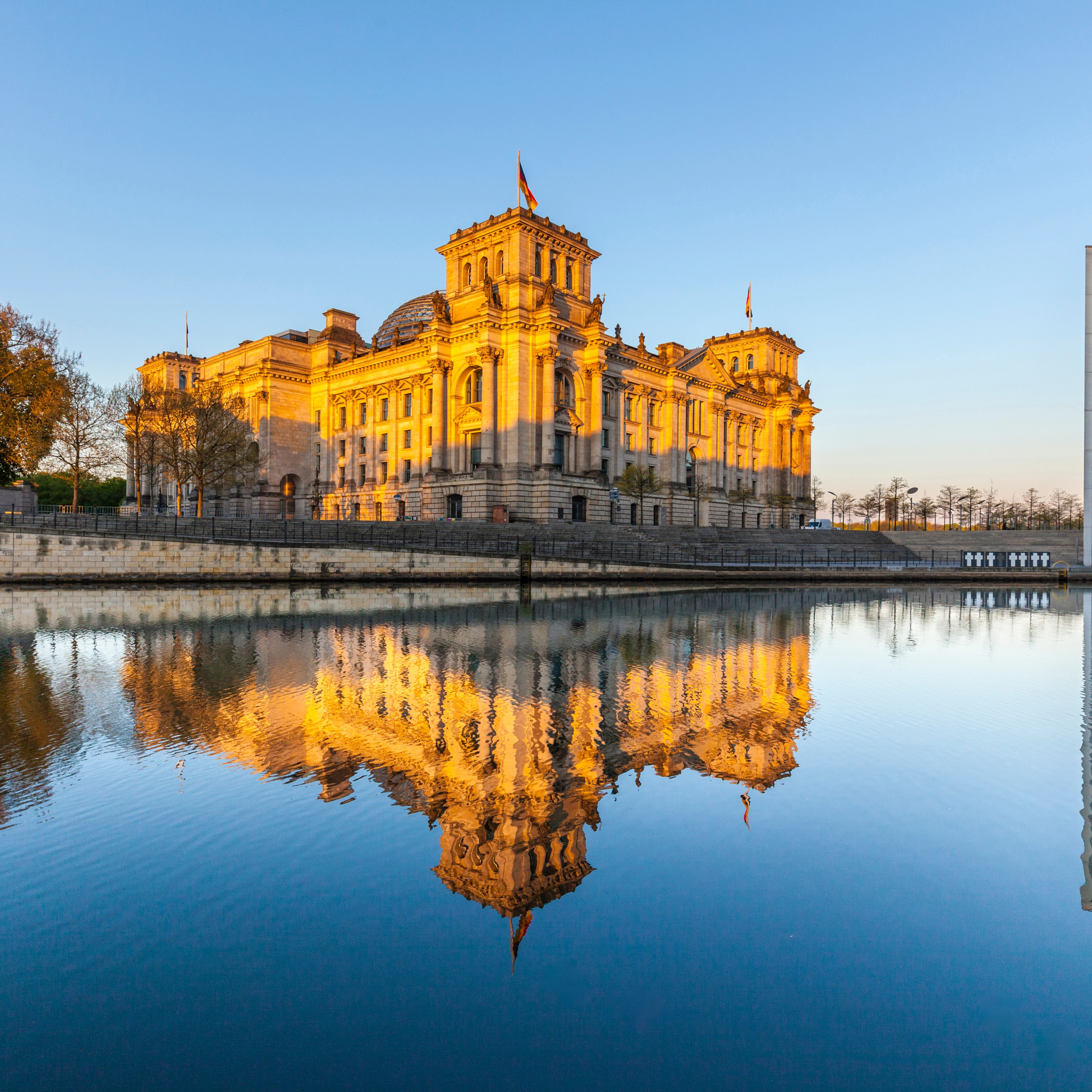 Das Berliner Reichstagsgebäude spiegelt sich im Fluss bei Sonnenuntergang.