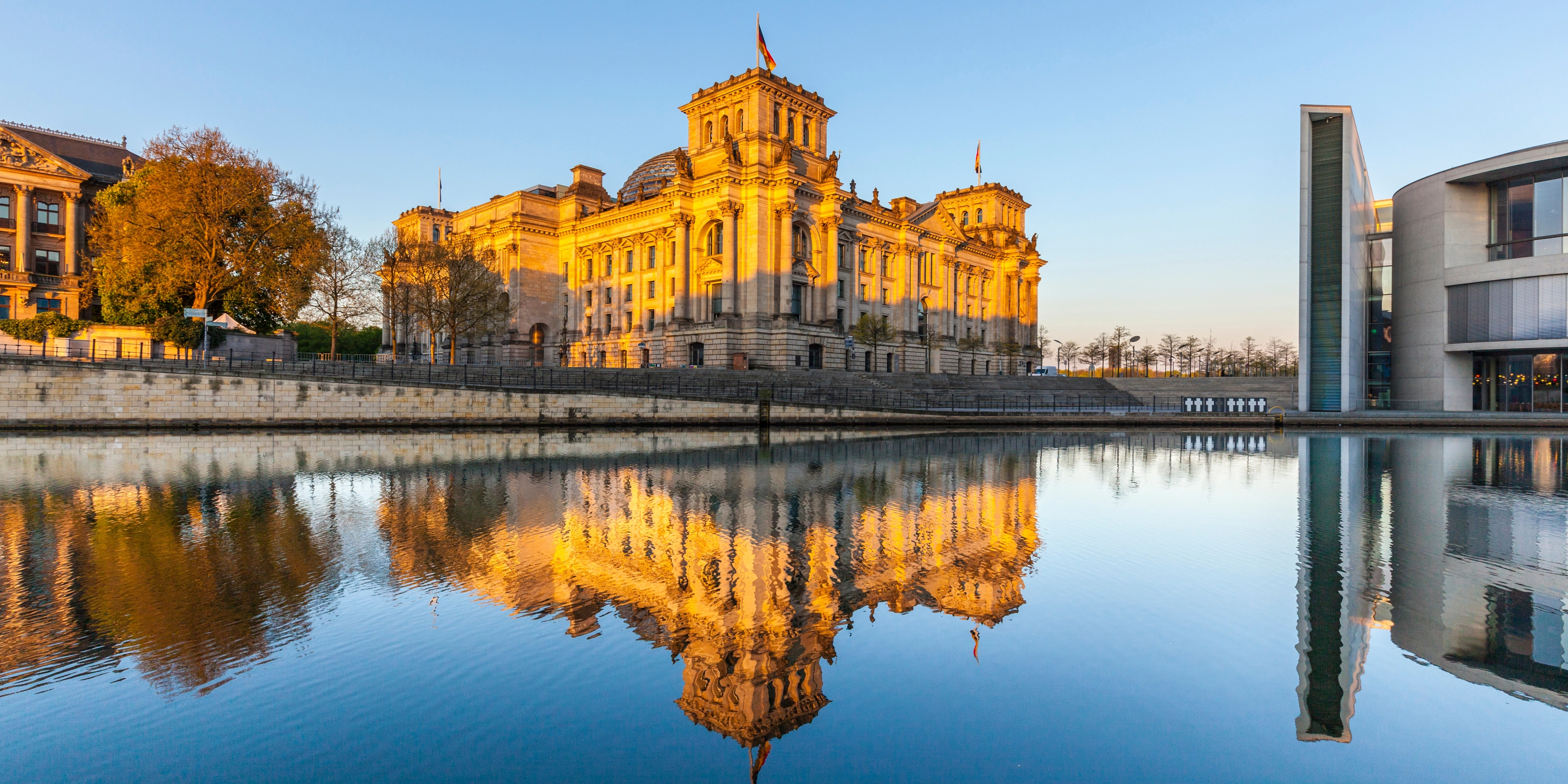 Das Berliner Reichstagsgebäude spiegelt sich im Fluss bei Sonnenuntergang.