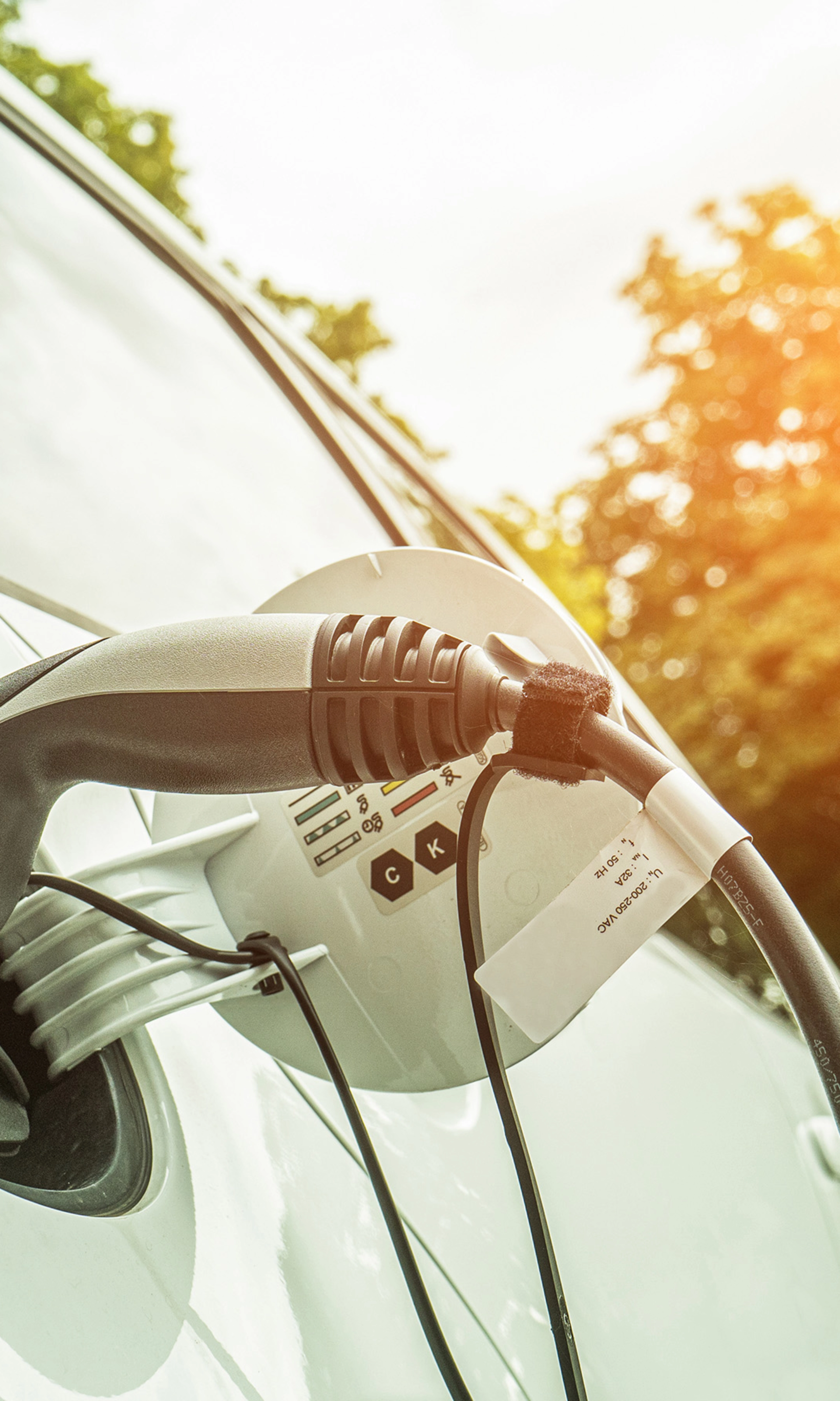 Elektroauto lädt im Freien bei Sonnenlicht, das Ladekabel steckt seitlich im Fahrzeug.