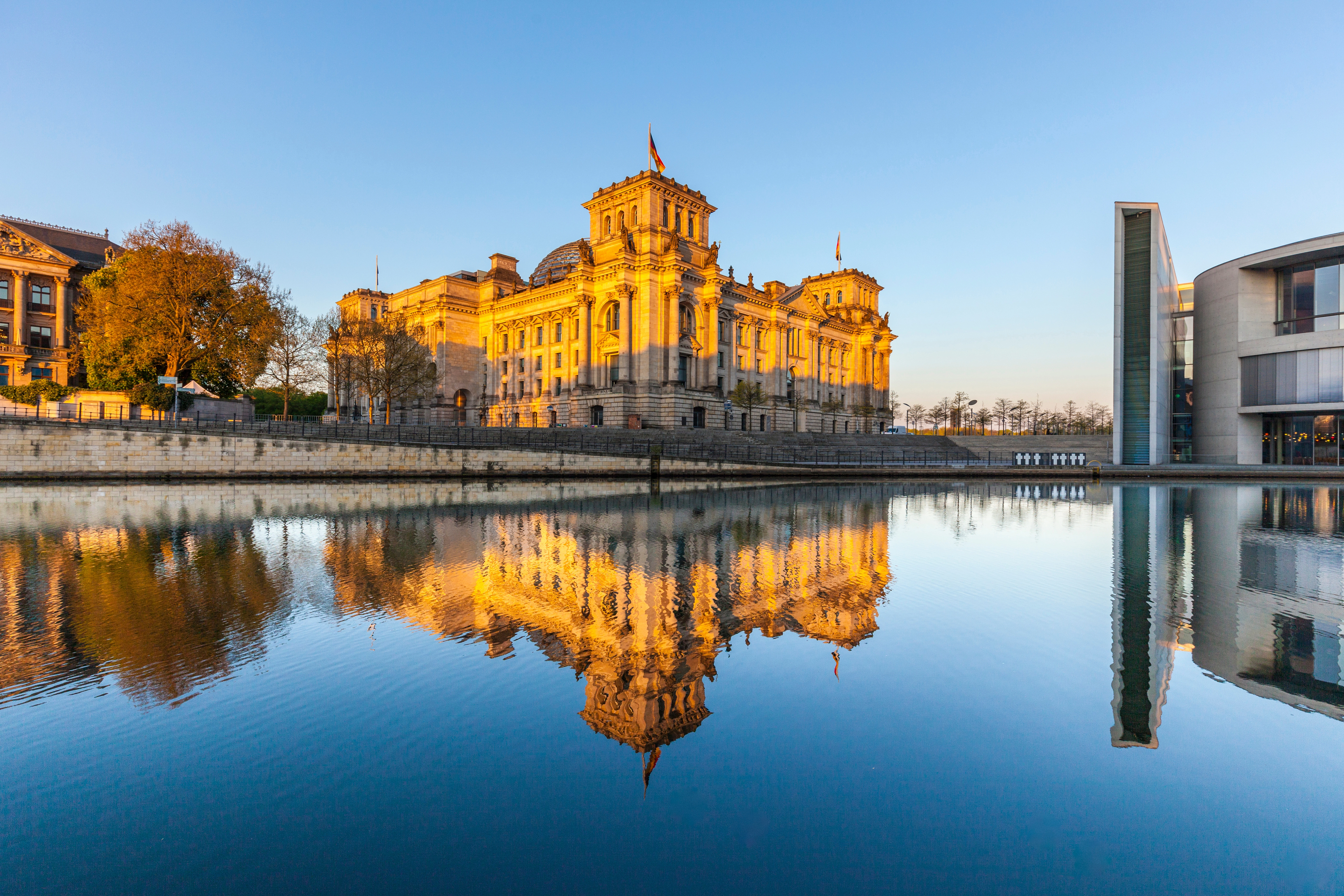 Das Berliner Reichstagsgebäude spiegelt sich im Fluss bei Sonnenuntergang.