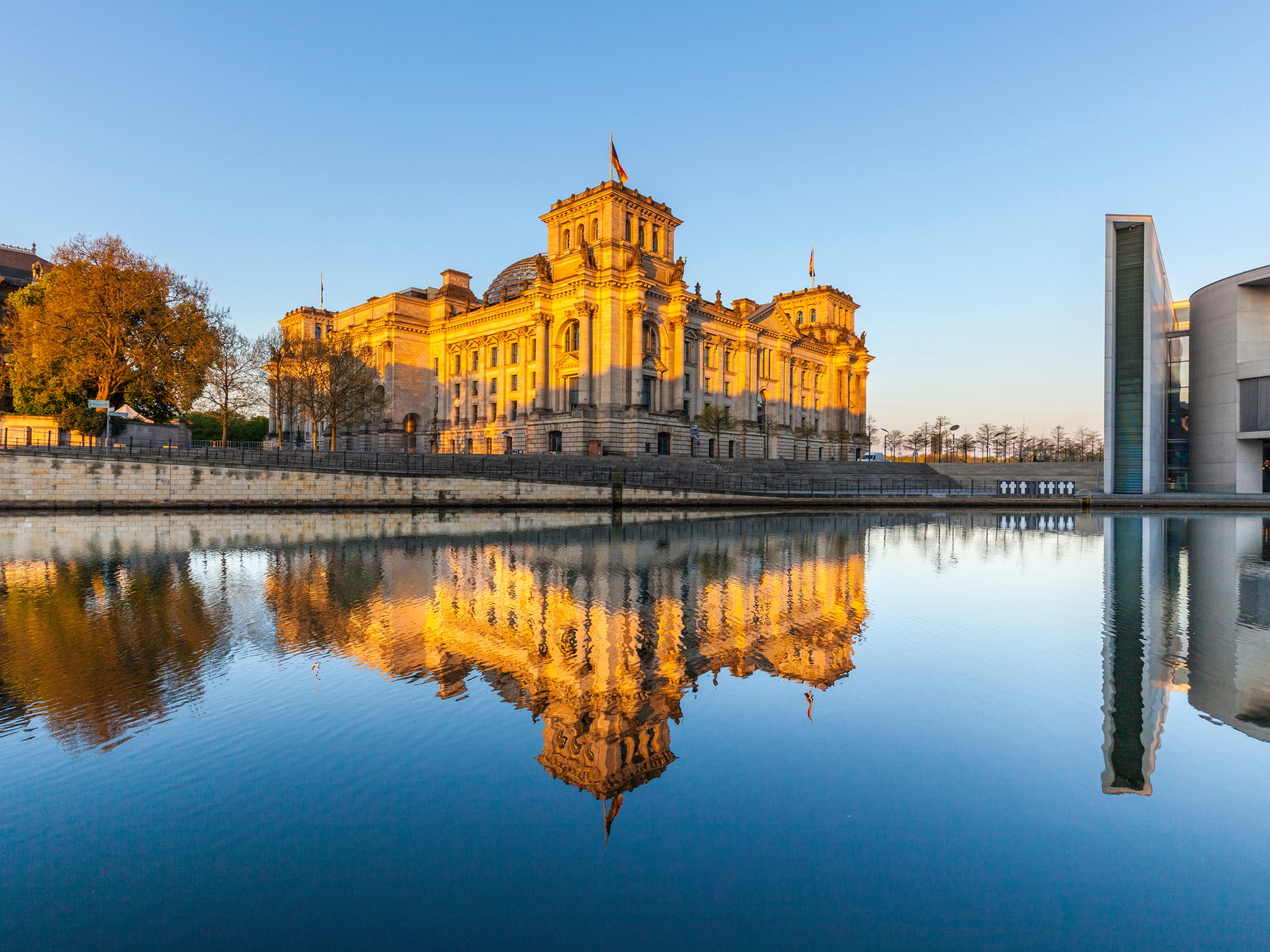 Das Berliner Reichstagsgebäude spiegelt sich im Fluss bei Sonnenuntergang.