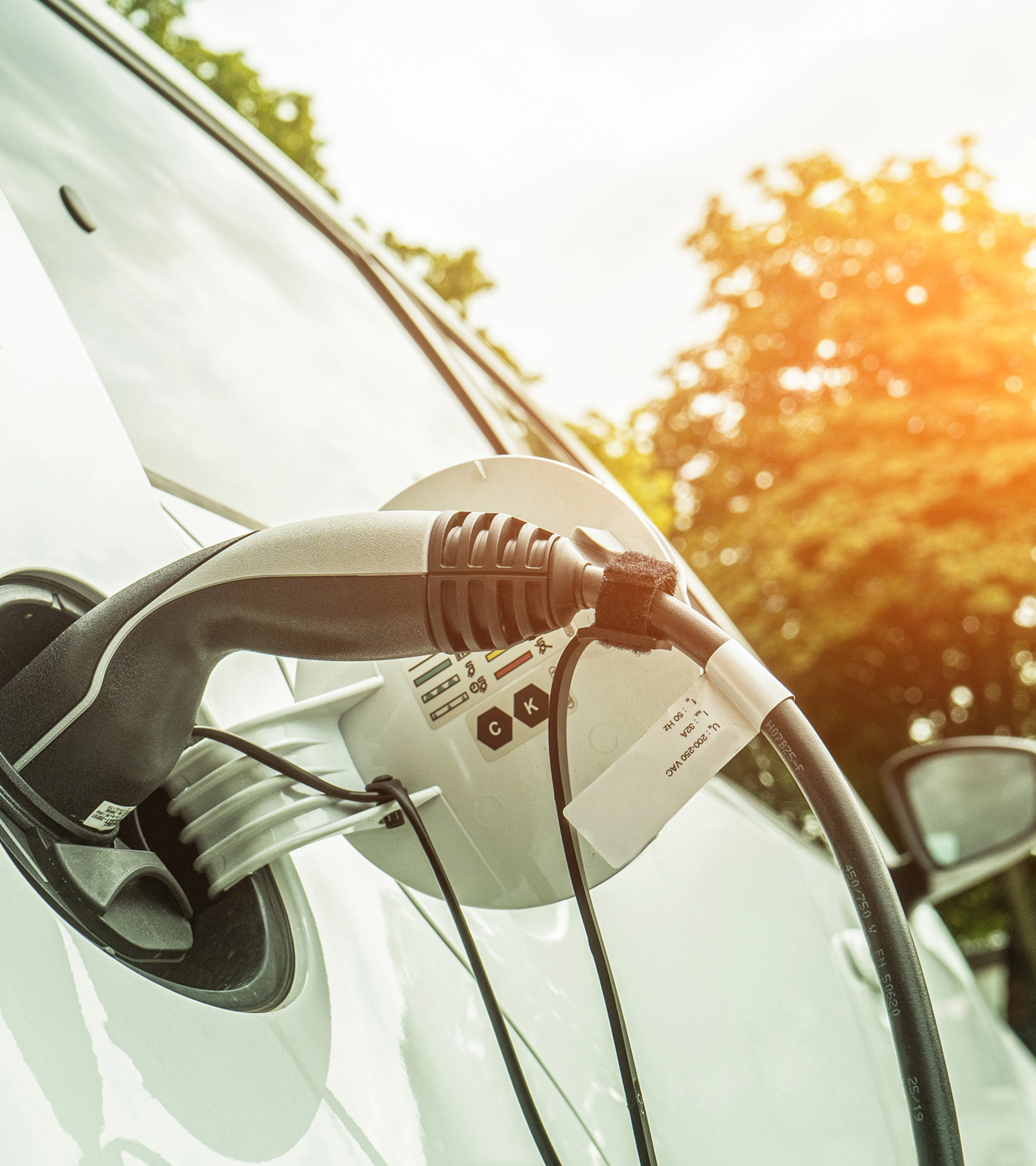 Elektroauto lädt im Freien bei Sonnenlicht, das Ladekabel steckt seitlich im Fahrzeug.