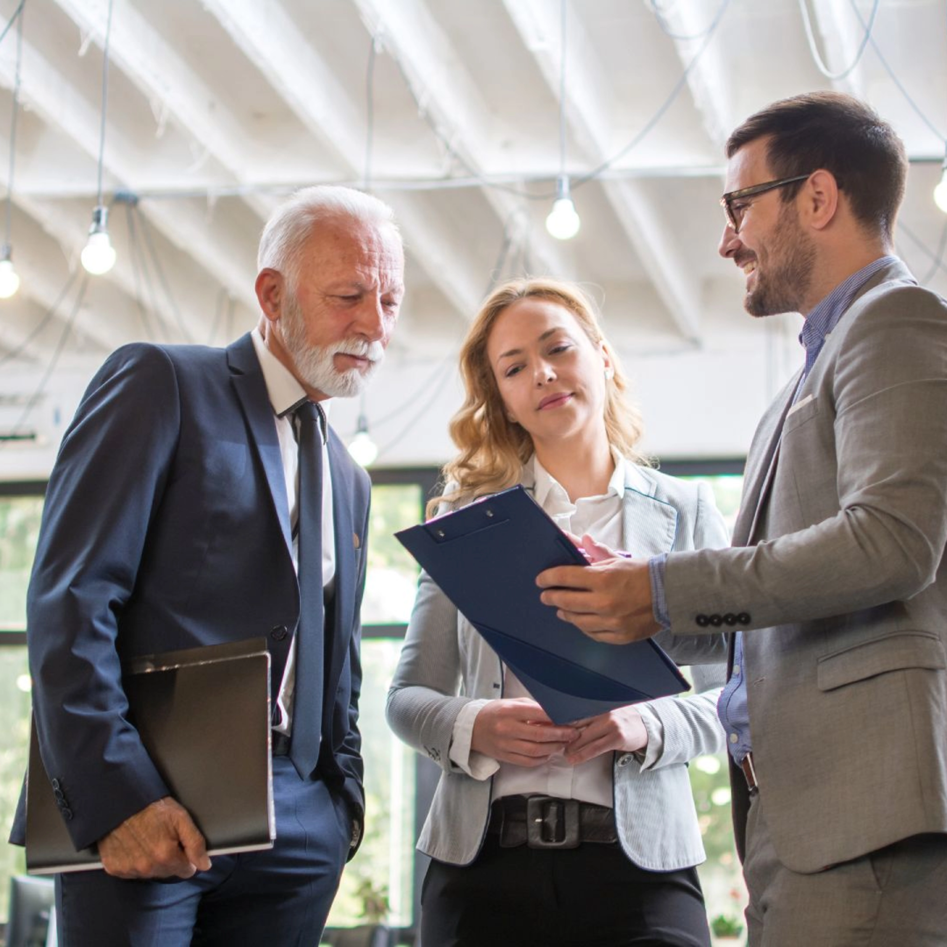Three people in business attire discussing a document in a modern office.