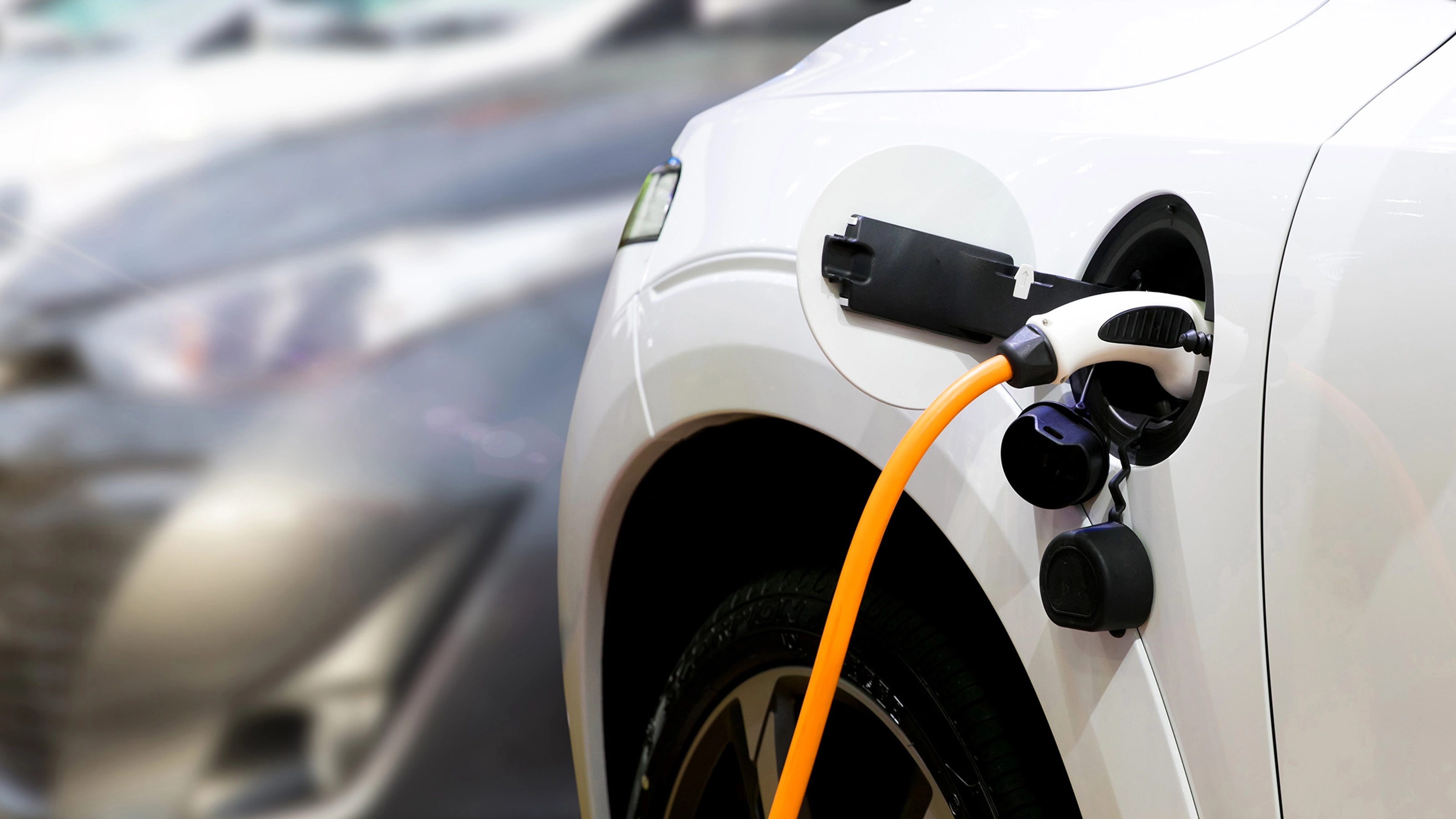 Nahaufnahme eines Elektroautos, das mit einem orangefarbenen Kabel geladen wird.