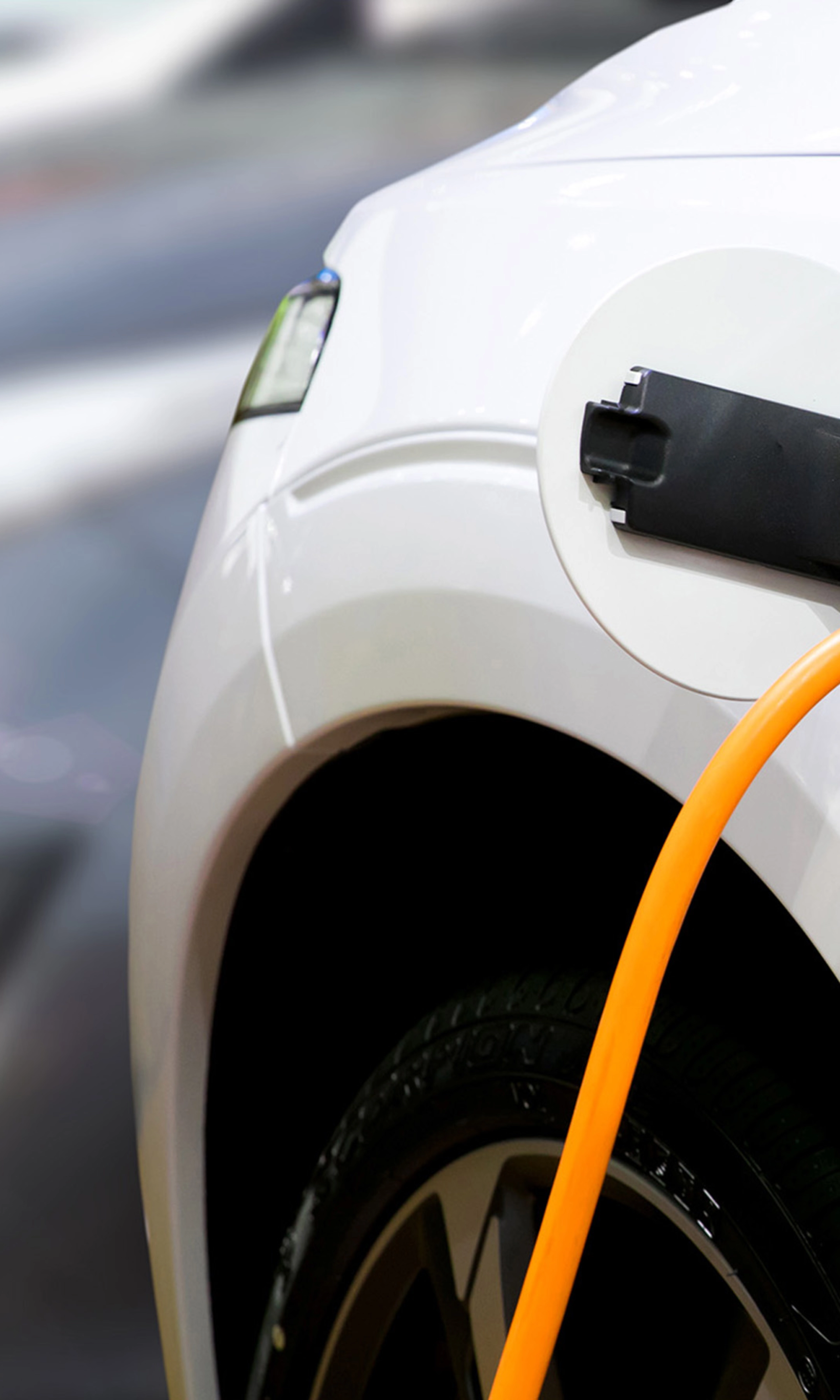 Nahaufnahme eines Elektroautos, das mit einem orangefarbenen Kabel geladen wird.