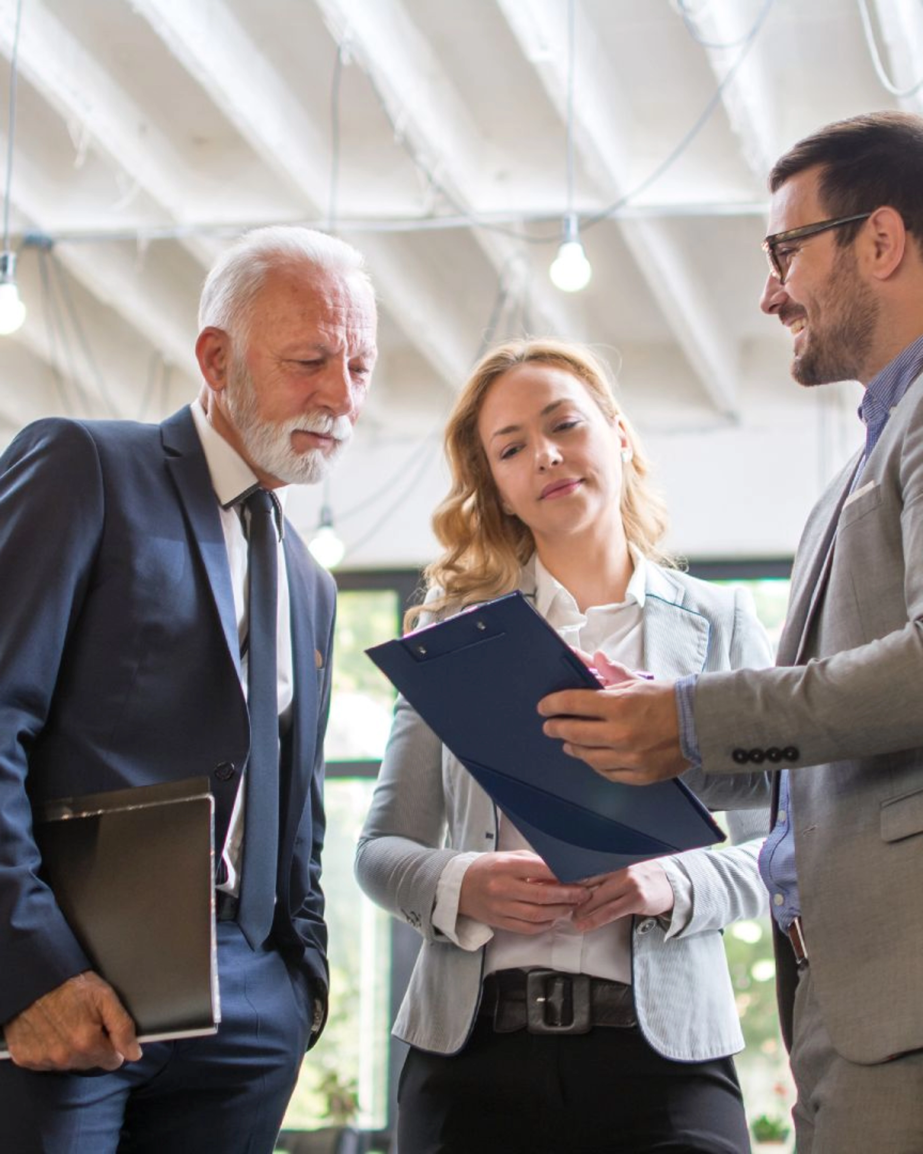 Three people in business attire discussing a document in a modern office.