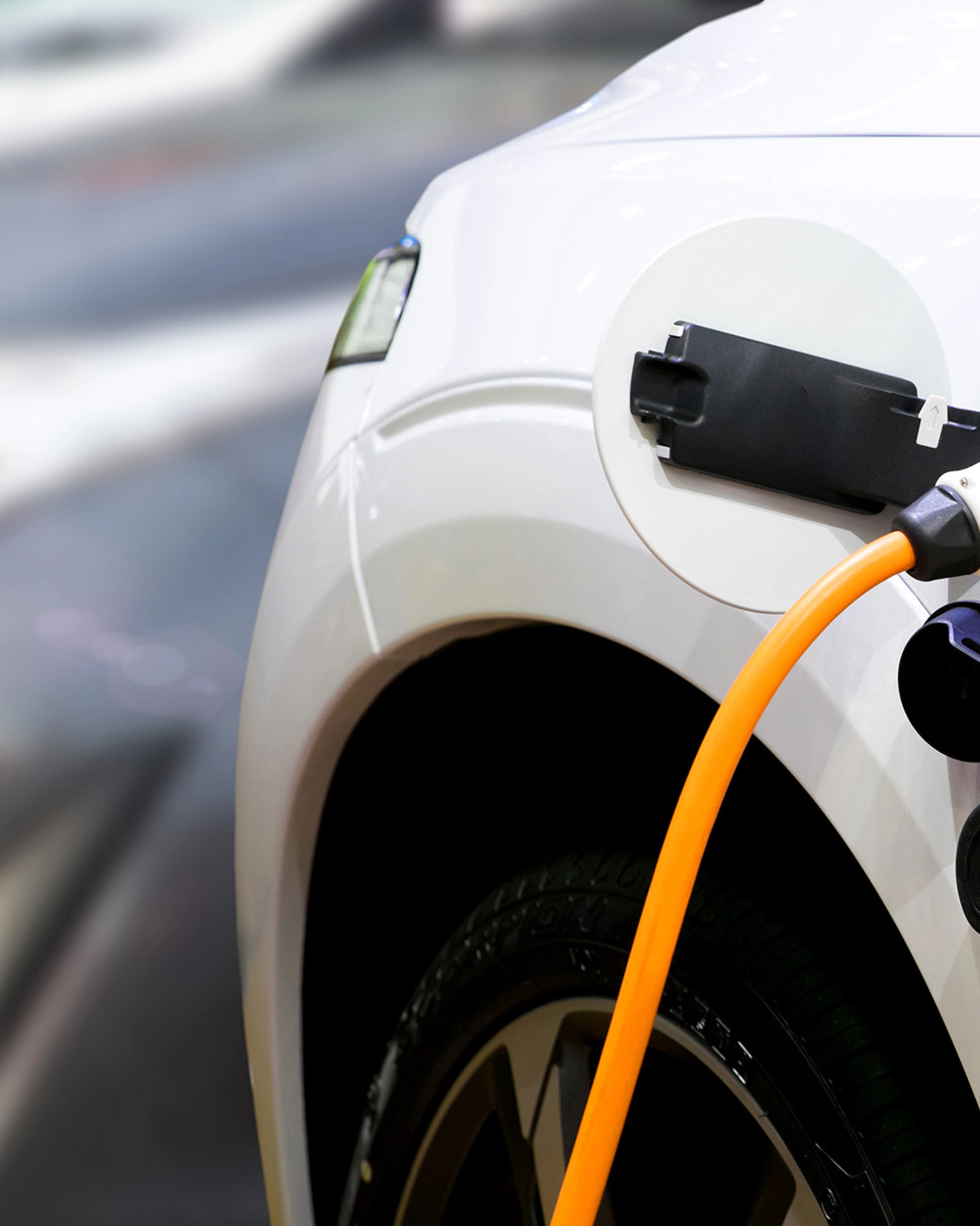 Nahaufnahme eines Elektroautos, das mit einem orangefarbenen Kabel geladen wird.