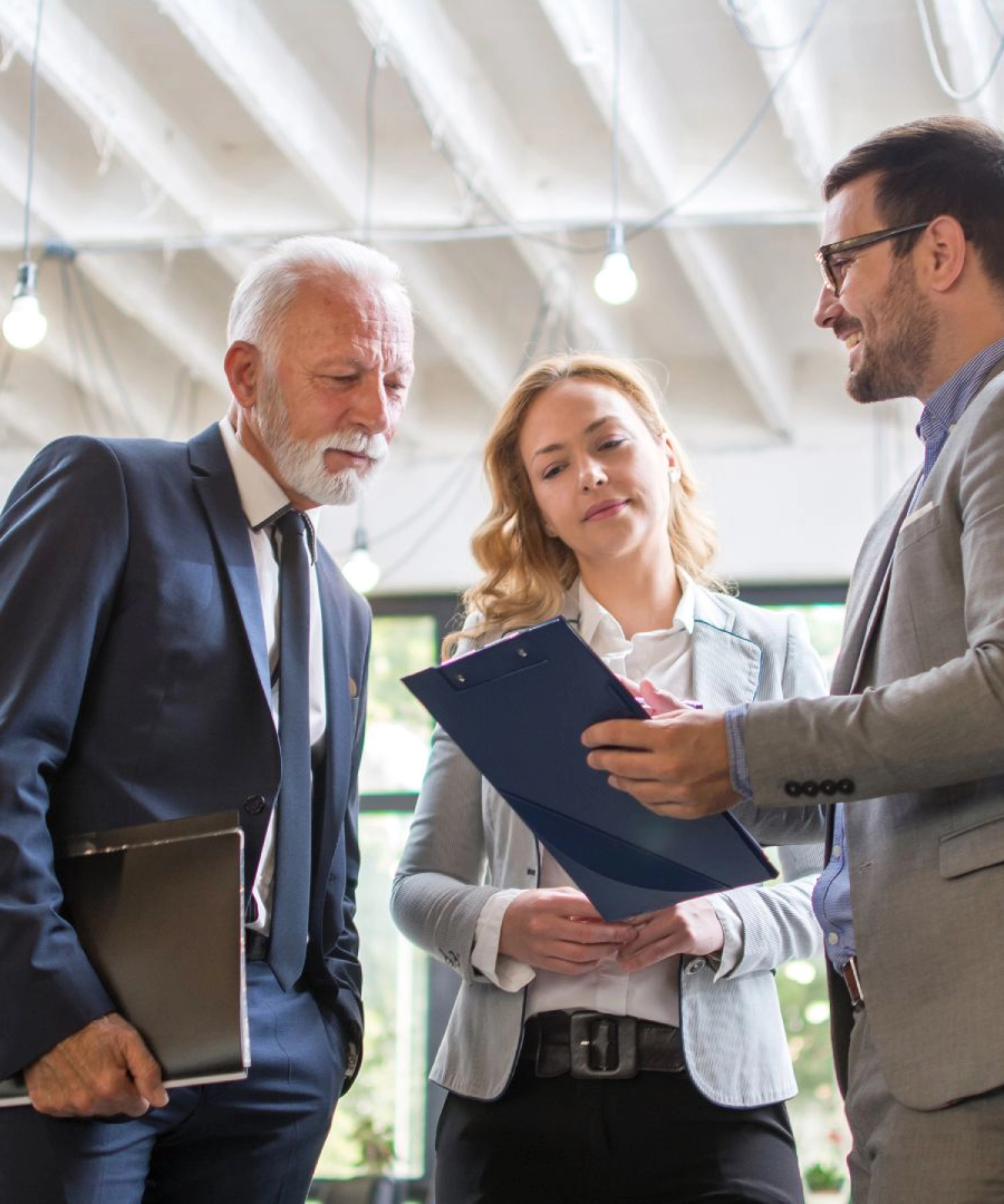 Three people in business attire discussing a document in a modern office.