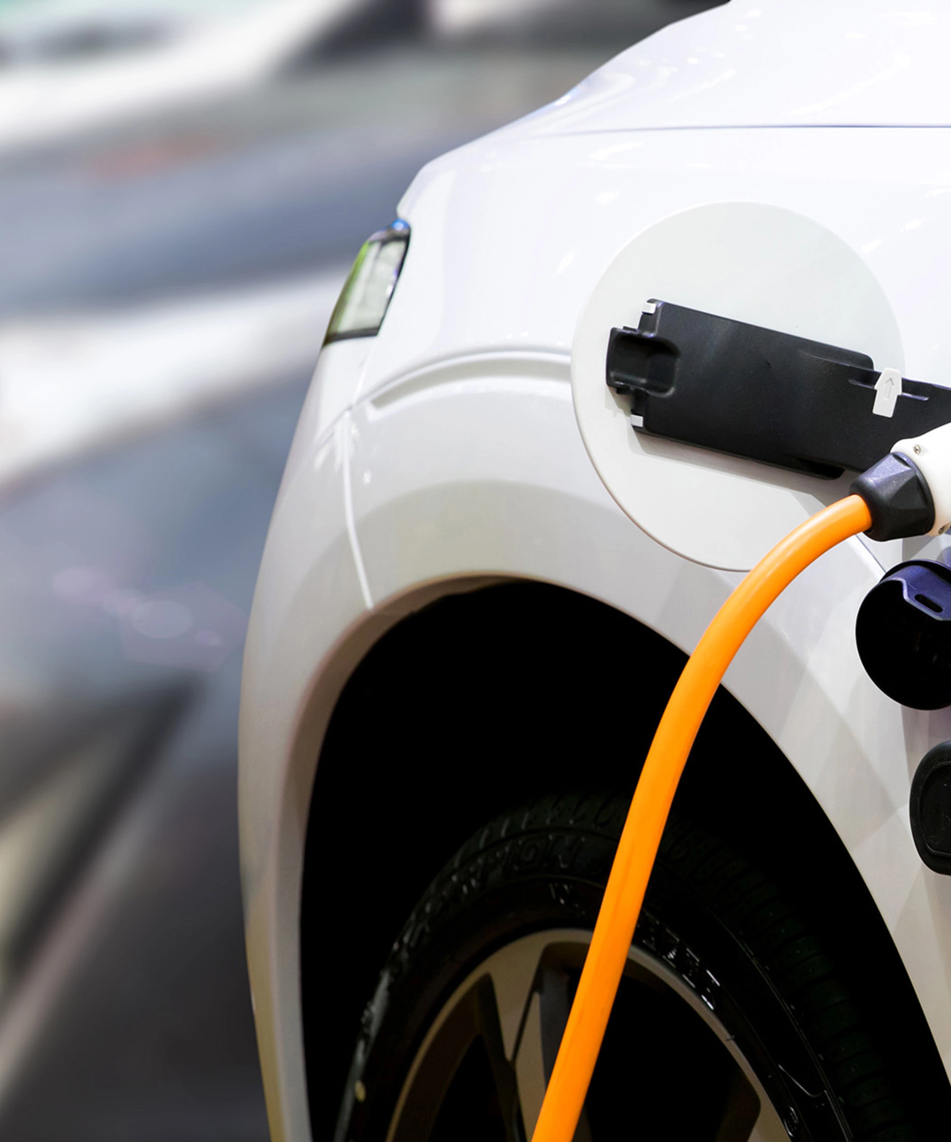 Nahaufnahme eines Elektroautos, das mit einem orangefarbenen Kabel geladen wird.