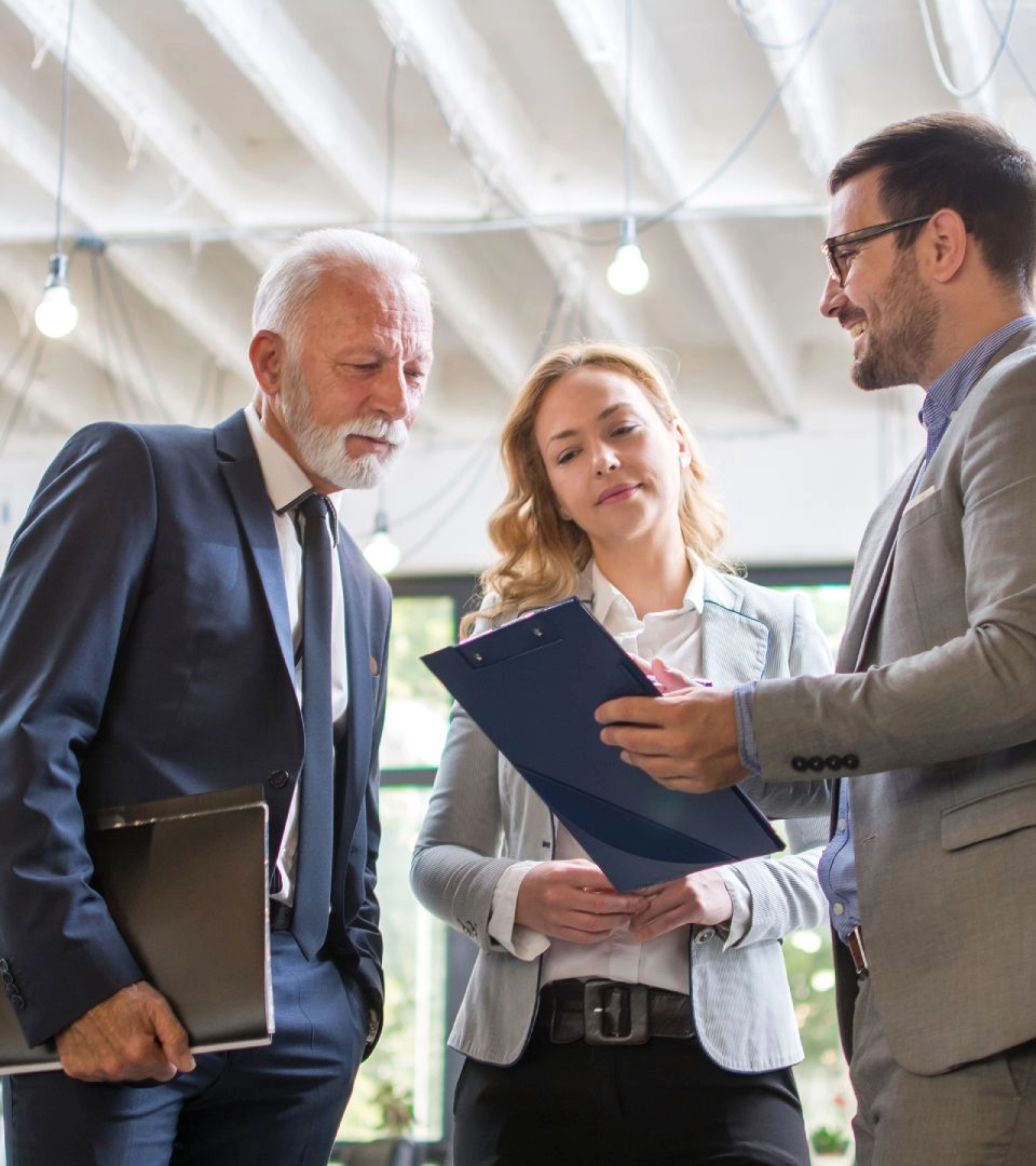 Three people in business attire discussing a document in a modern office.