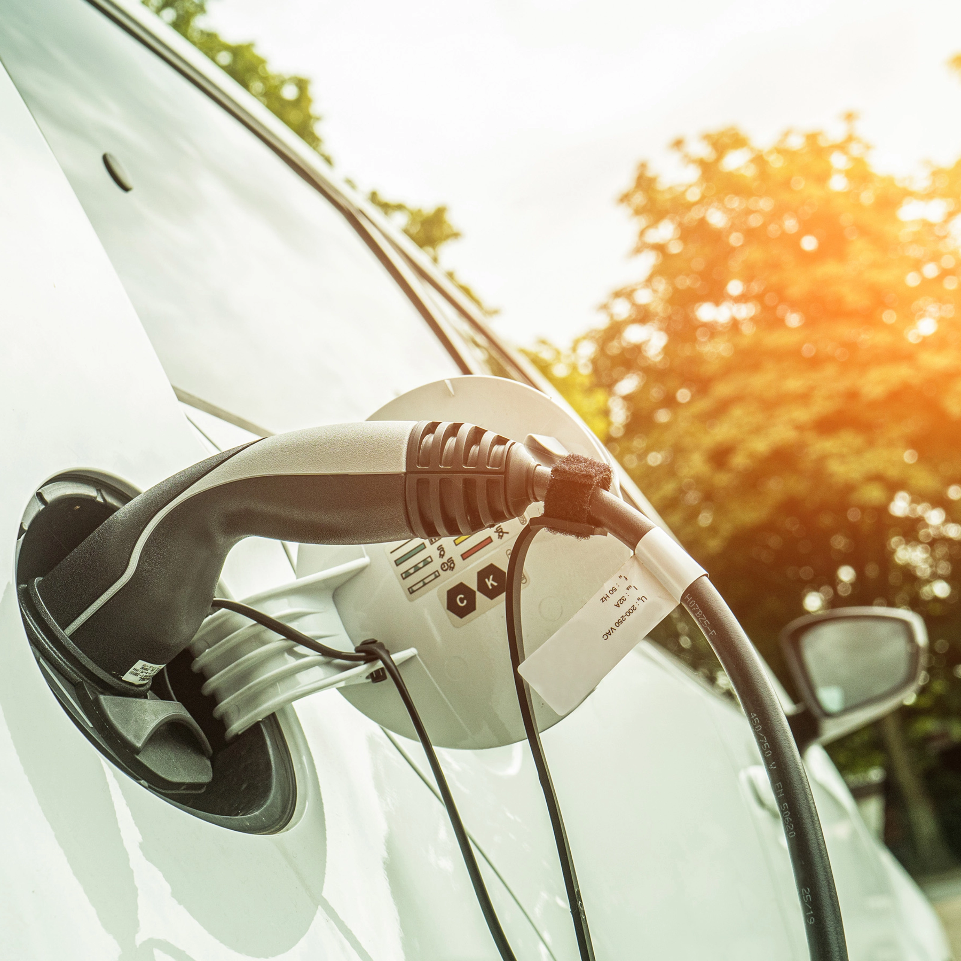 Elektroauto lädt im Freien bei Sonnenlicht, das Ladekabel steckt seitlich im Fahrzeug.