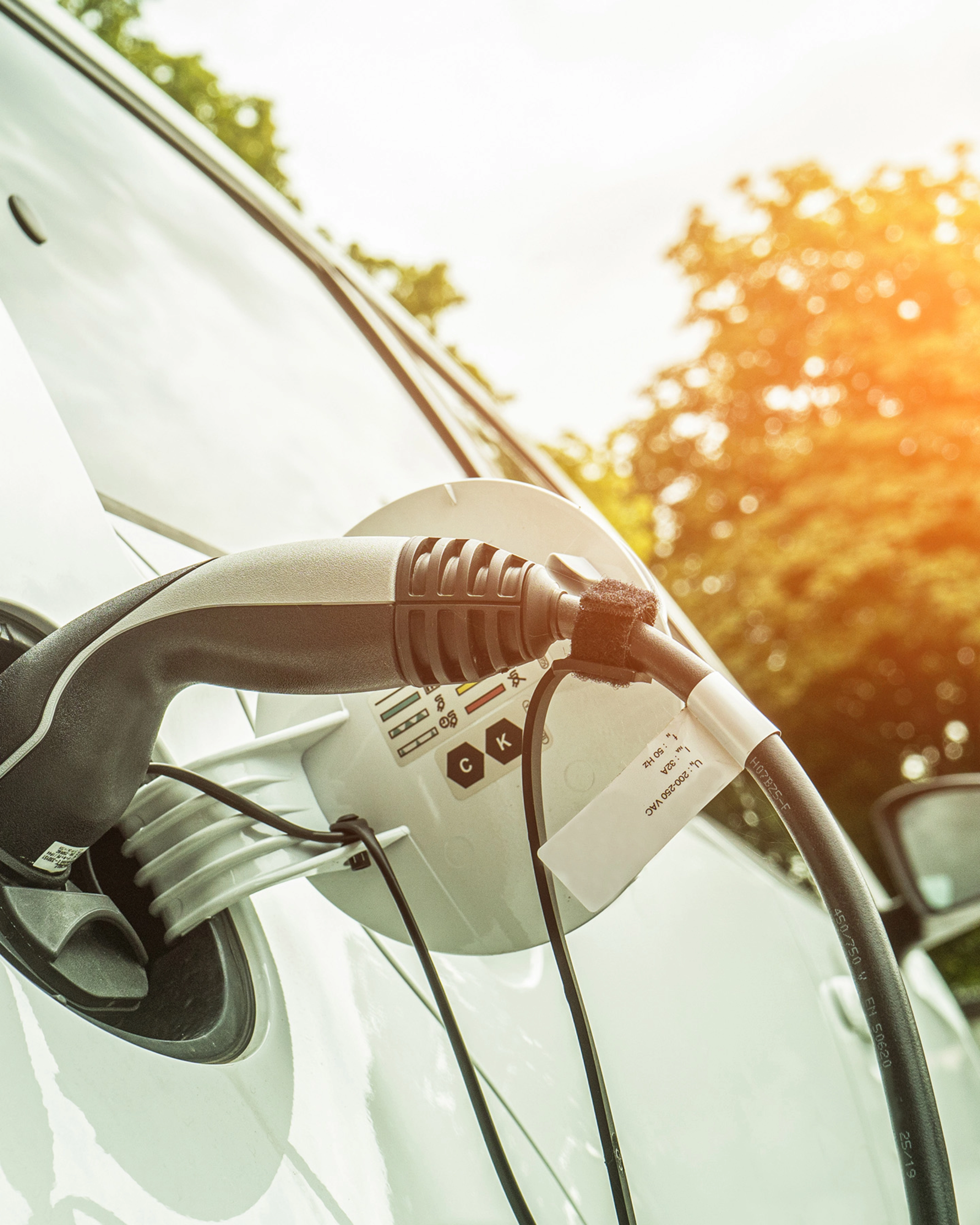 Elektroauto lädt im Freien bei Sonnenlicht, das Ladekabel steckt seitlich im Fahrzeug.