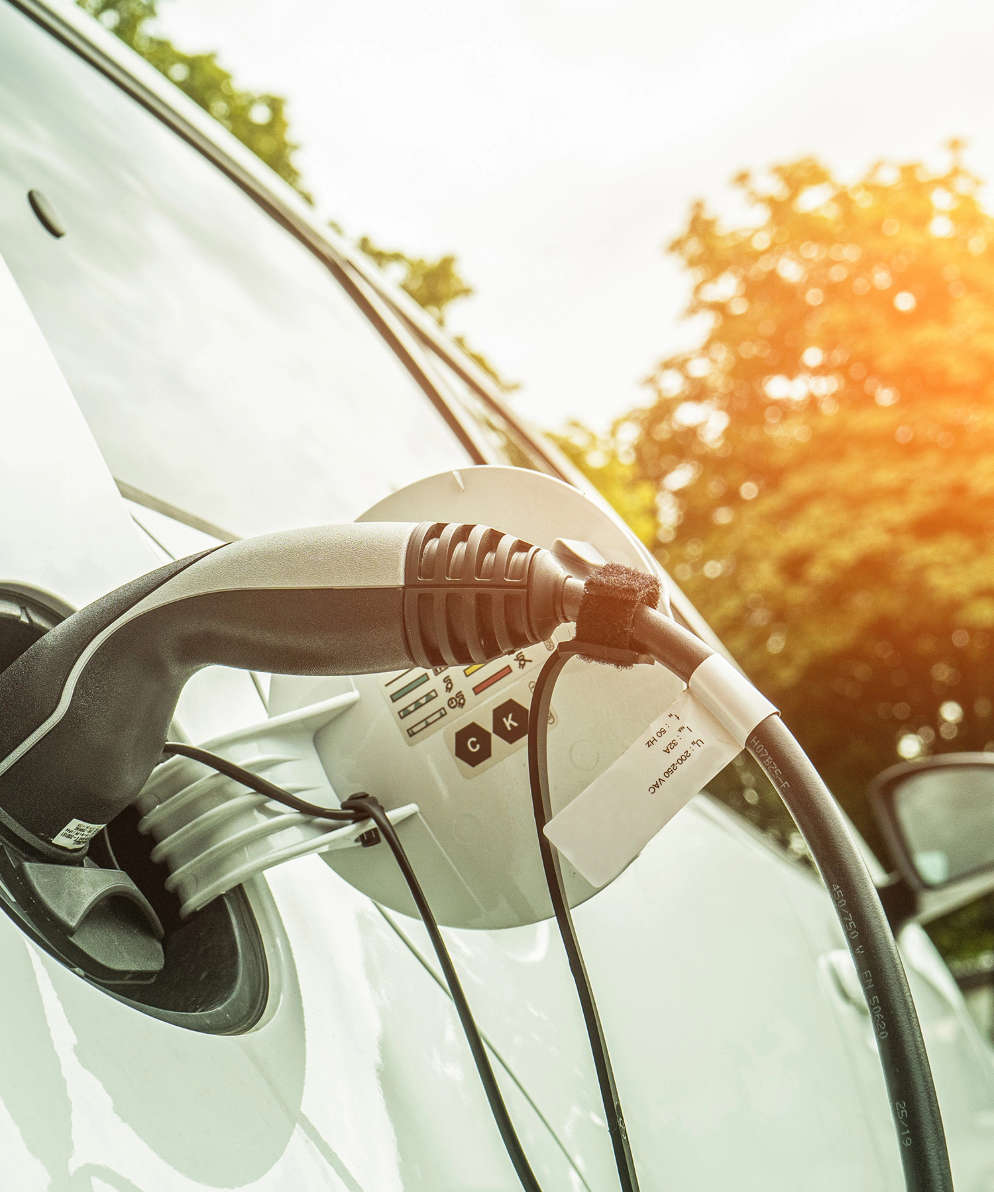 Elektroauto lädt im Freien bei Sonnenlicht, das Ladekabel steckt seitlich im Fahrzeug.